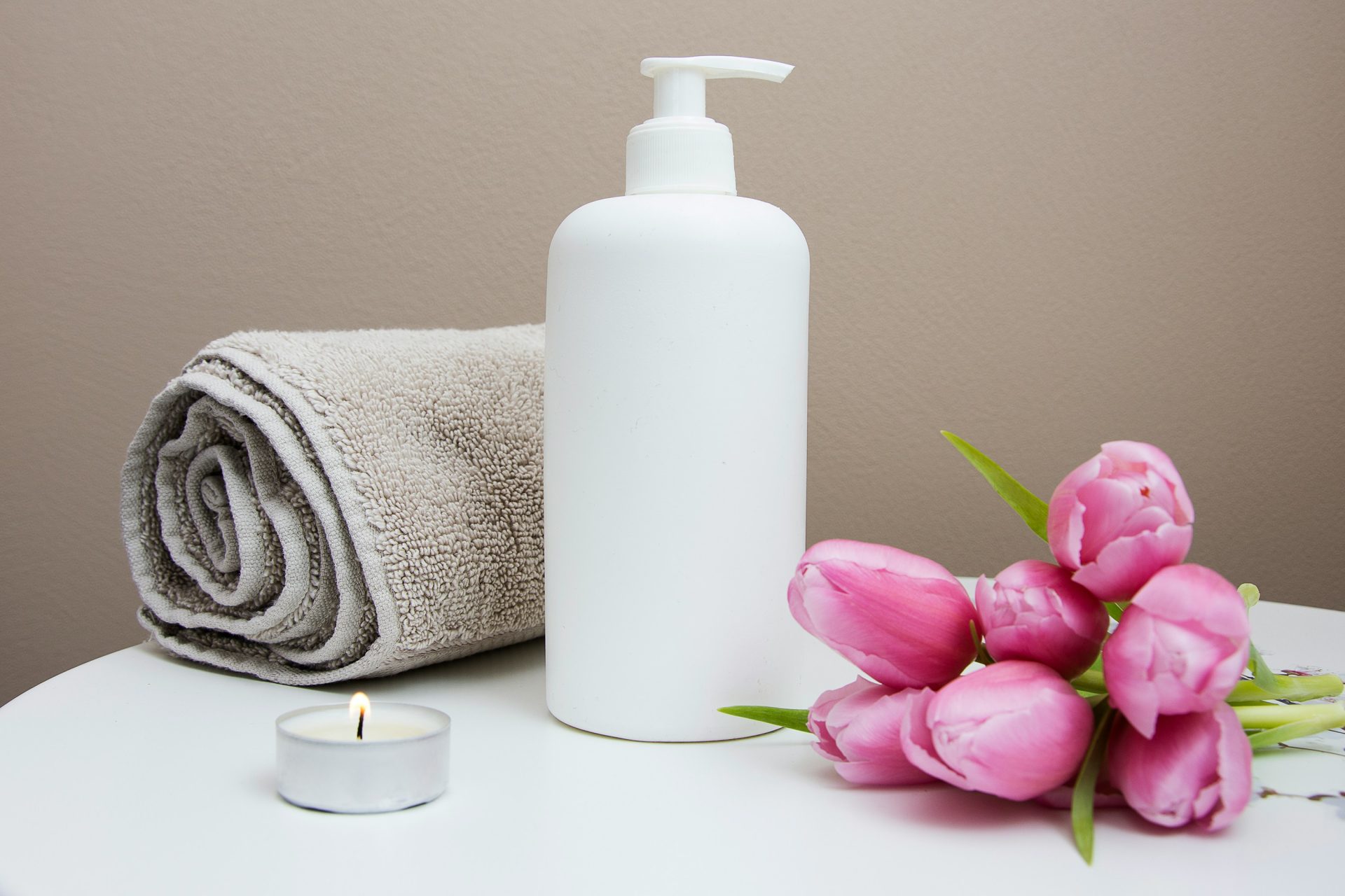 Towel, lotion, candle, and pink flowers.